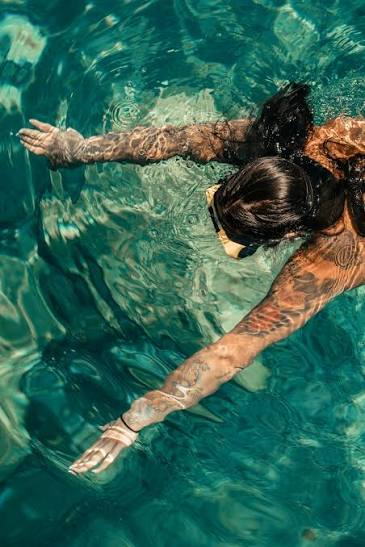 Von oben aufgenommene Schwimmerin mit ausgebreiteten Armen in türkisfarbenem Wasser.