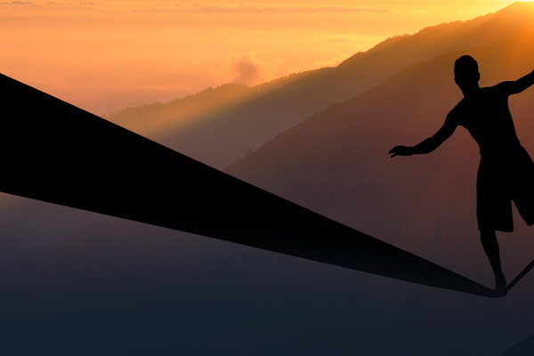 Silhouette einer Person, die bei Sonnenuntergang über einer Hügelkette auf einer Slackline balanciert.
